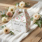Floral baby shower favor box with 'thank you' text on a wooden surface with flowers.