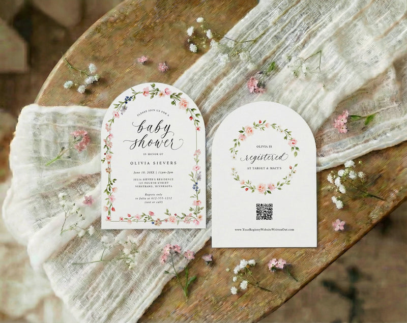 Baby shower invitations with floral designs on a wooden surface with baby's breath flowers.