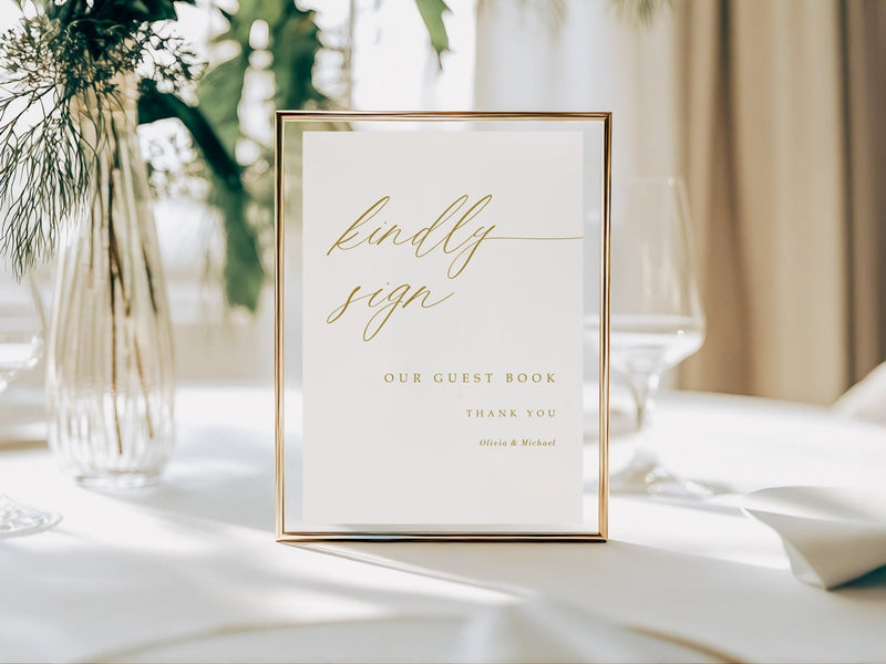Guest book sign with gold text on a white background, placed on a table with decorative elements.