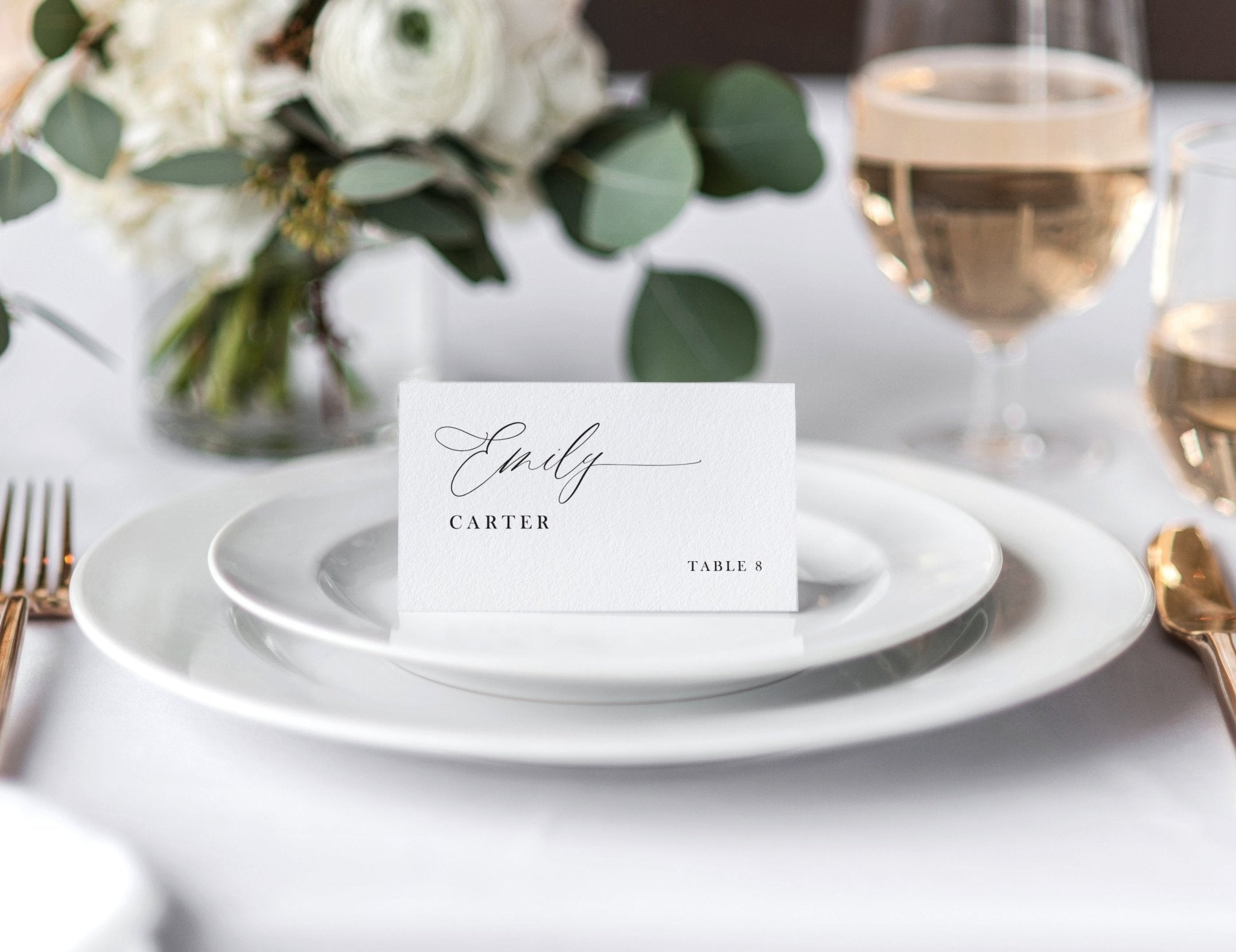 Modern romantic printed place card with guest name and table number, styled on a white plate at a wedding reception.