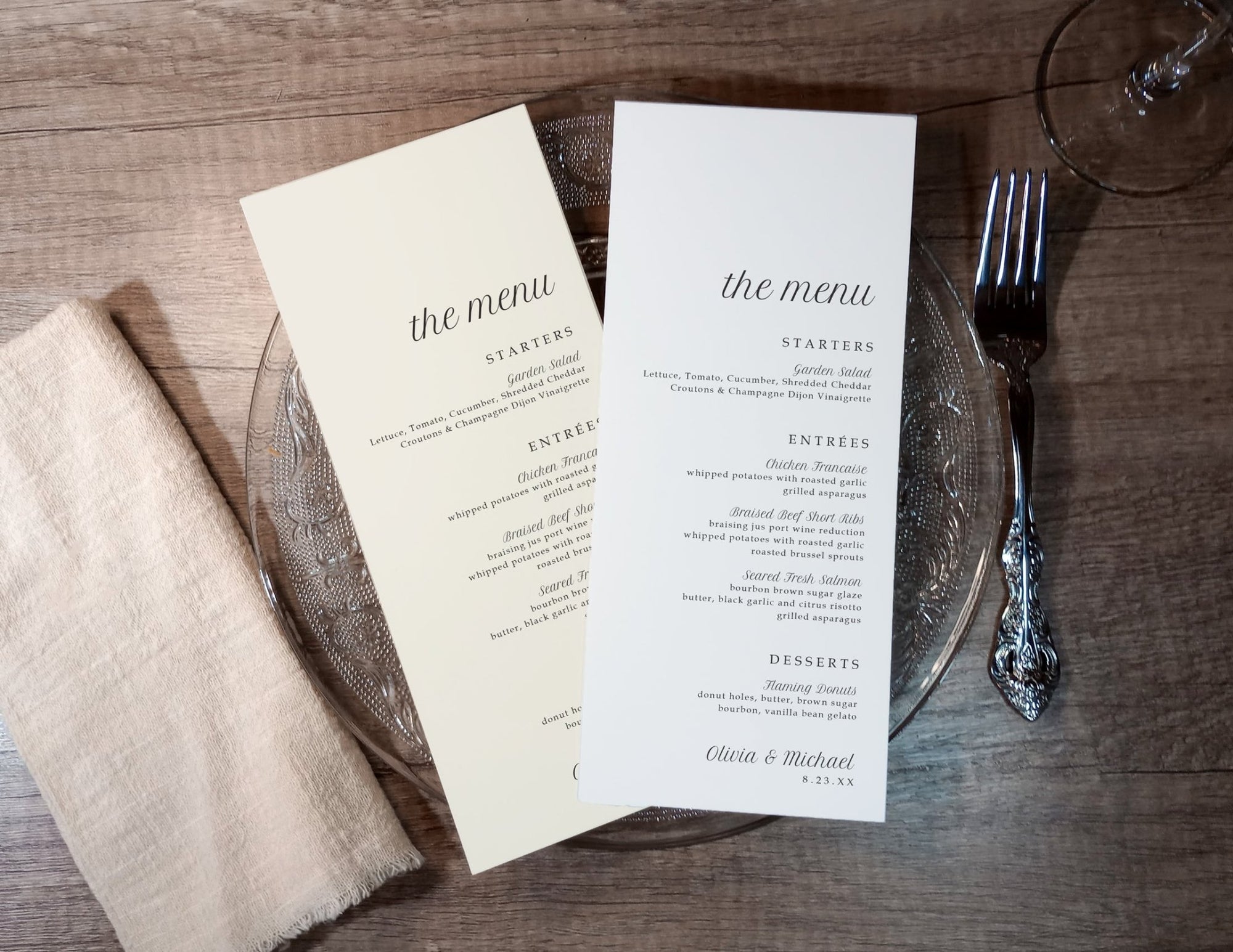 Two menu cards on a wooden table with a fork and glass.
