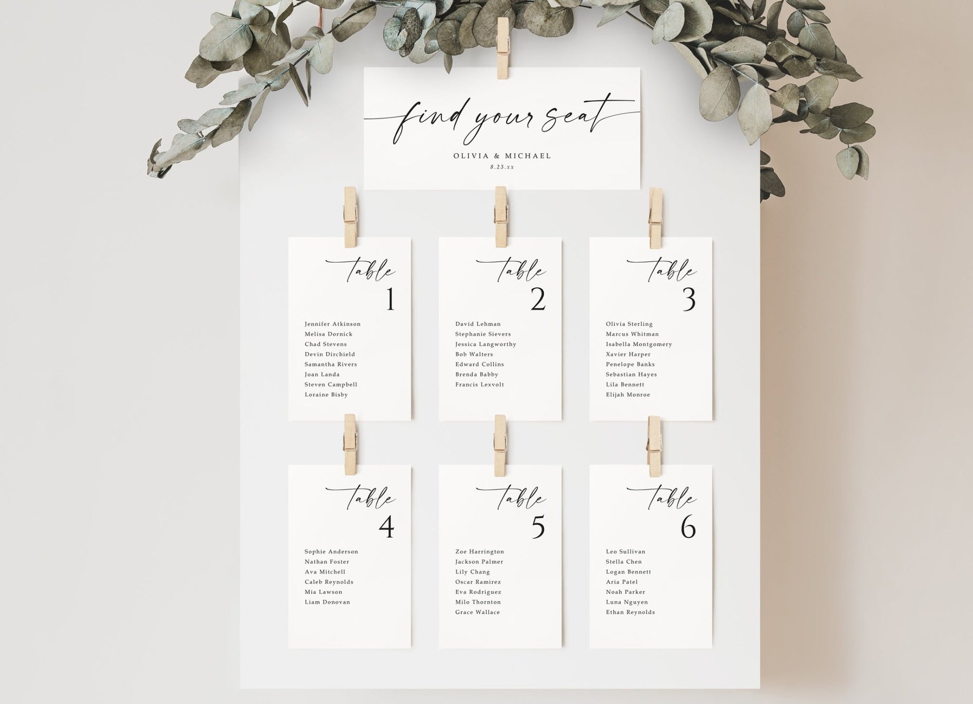 Wedding seating chart display with individual printed cards arranged under a custom header card with greenery accent.