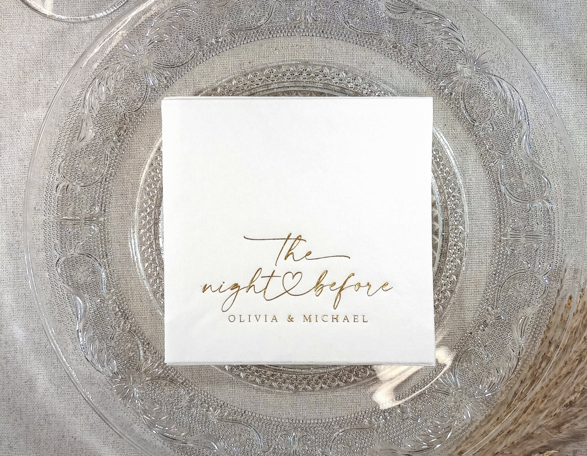 White cocktail napkin with “the night before” in black script and a hand-drawn heart, personalized with the couple’s names.