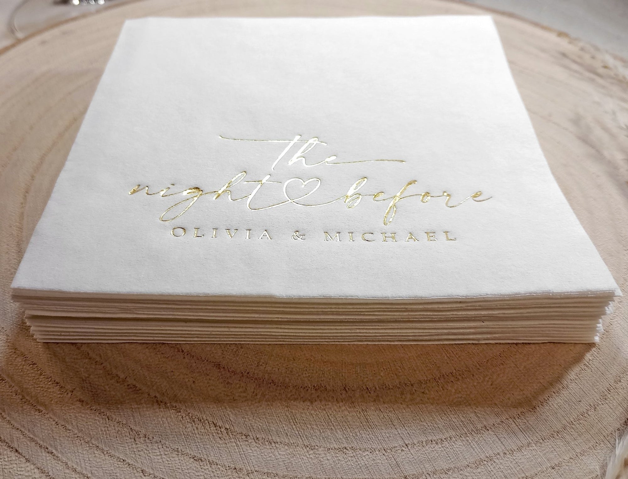 Stack of white napkins with gold text on a wooden surface