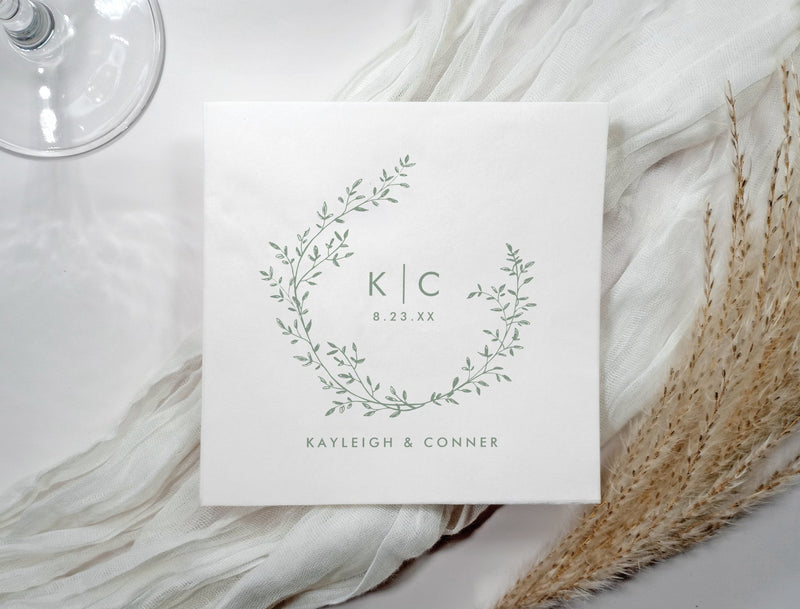 Sage green wedding napkin with botanical wreath, monogram initials, names, and date.