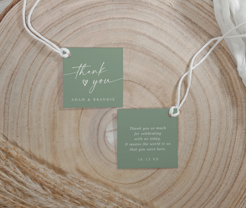 Two sage green tags with 'thank you' messages on a wooden surface
