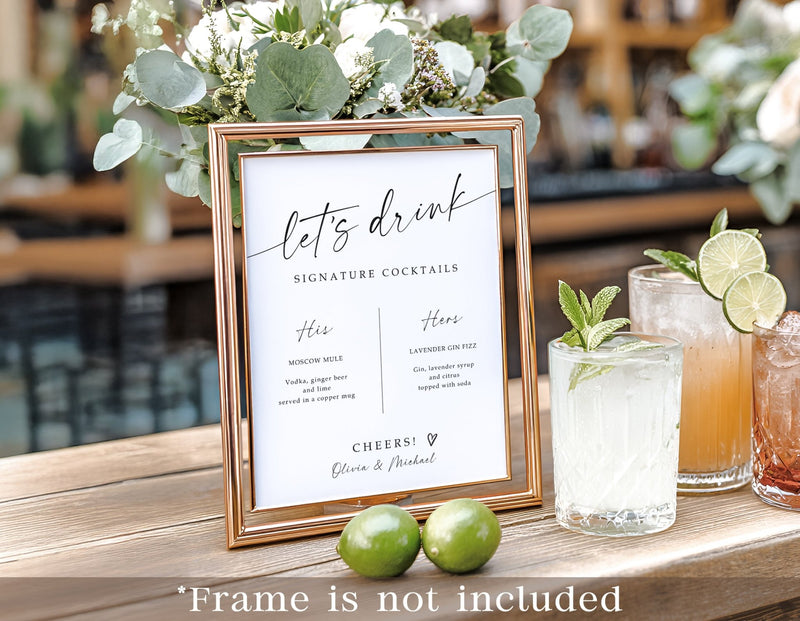 Signature drinks wedding sign in elegant handwriting displayed in a gold frame with cocktails beside it
