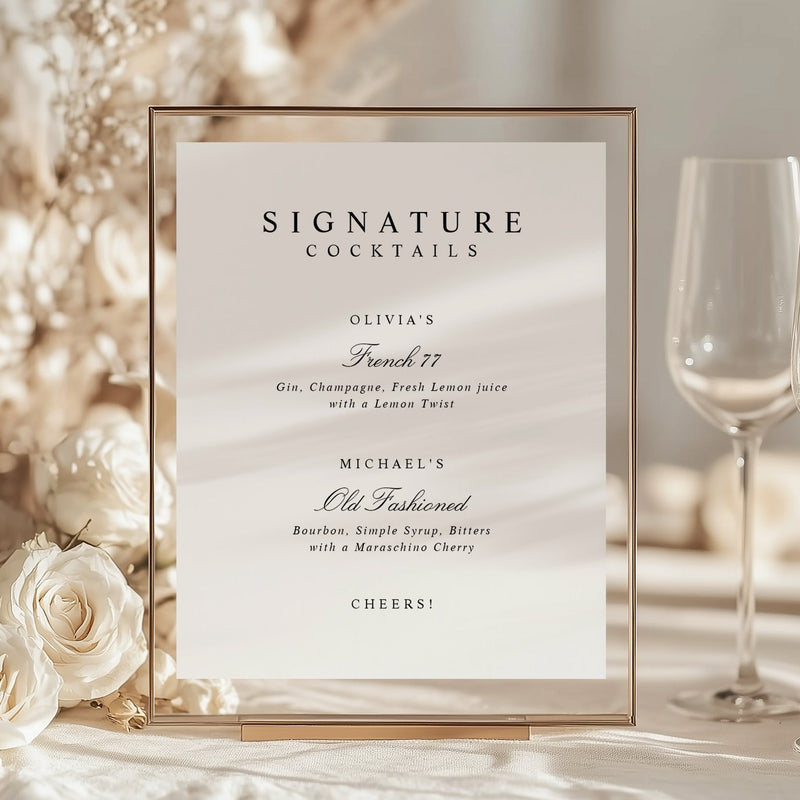 Framed signature cocktails menu with wine glasses and bottle on a decorative table.