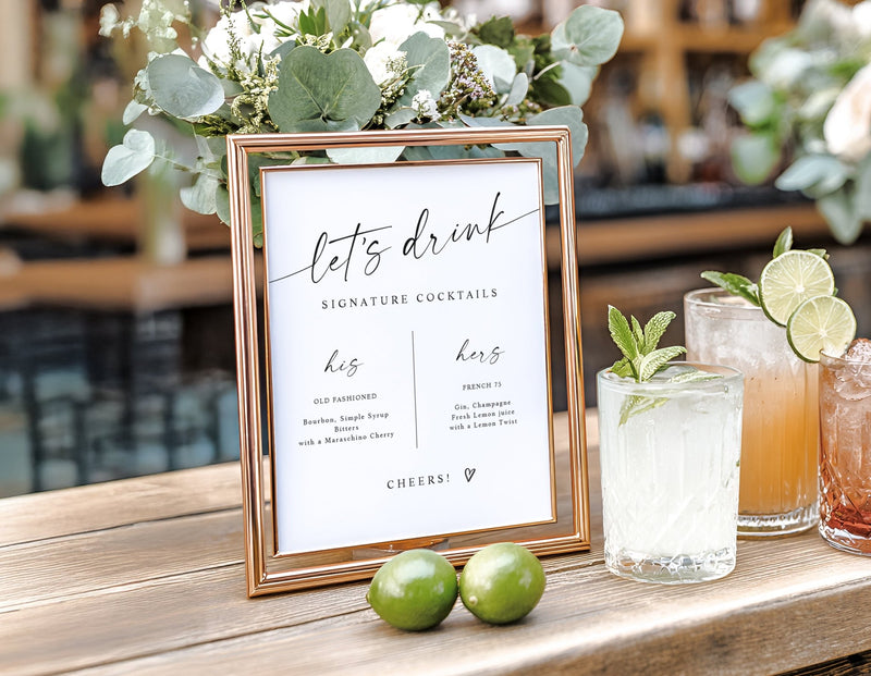 Signature drinks wedding sign in elegant handwriting displayed in a gold frame with cocktails beside it