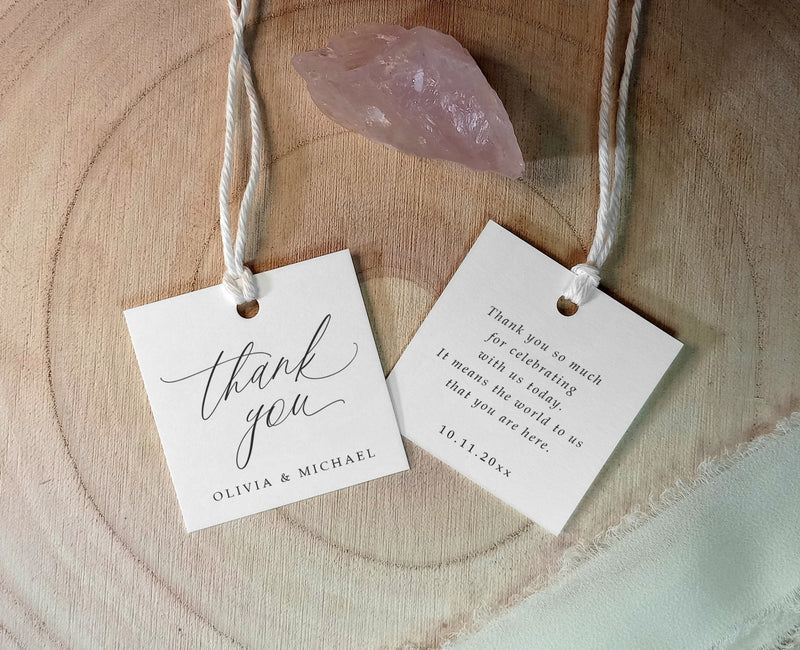 Two 'thank you' tags hanging on a wooden surface with a pink crystal.