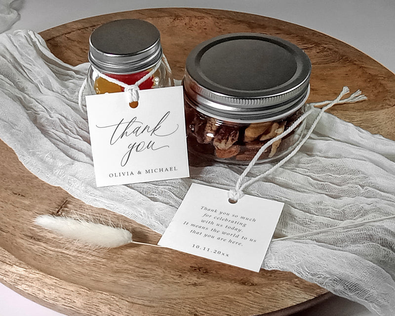 Two jars with silver lids on a wooden surface with 'thank you' tags.