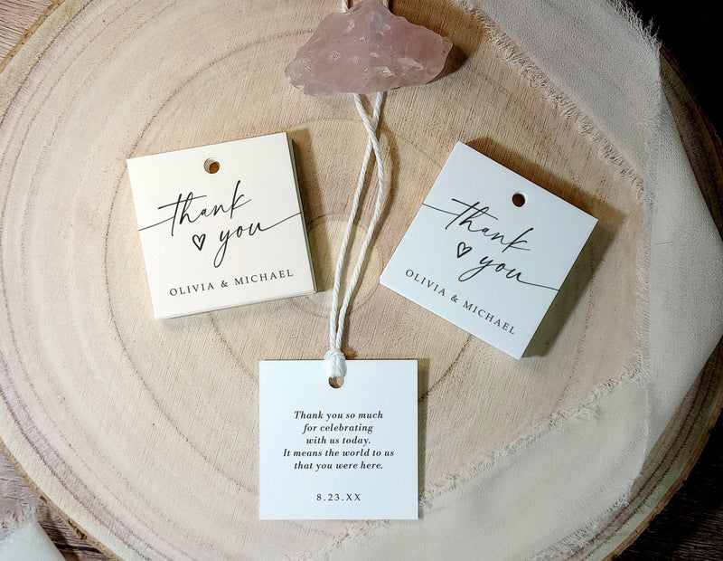 Three 'thank you' tags on a wooden surface with a decorative stone.
