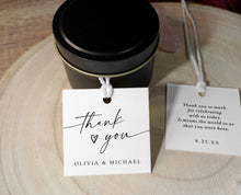 Candle in a black tin with 'thank you' tag on a wooden surface