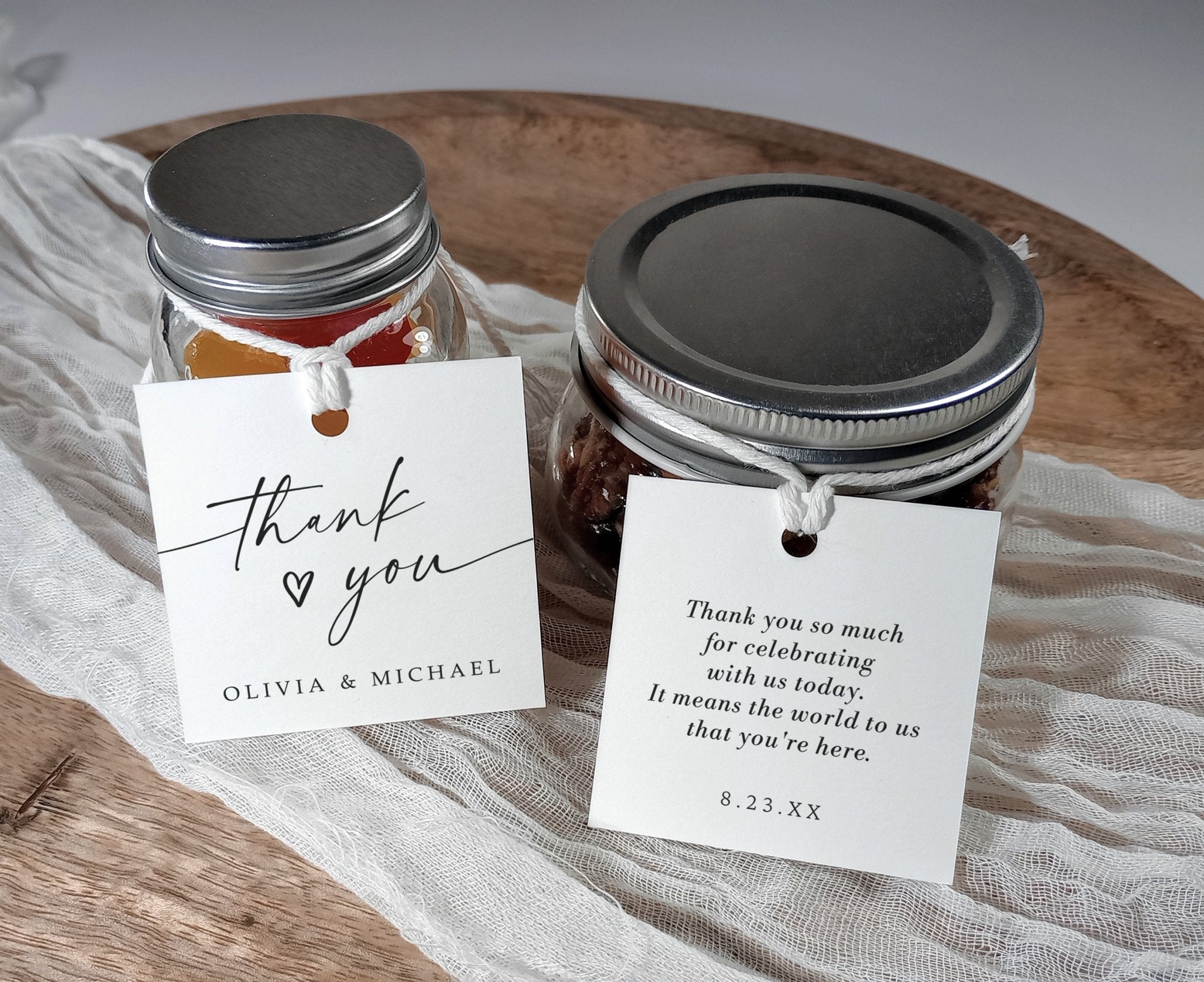 Two jars with metal lids on a wooden surface, each with a personalized thank you tags.