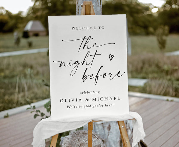 White foam board sign that says "the night before" with hand-drawn heart and custom names on a scenic background.