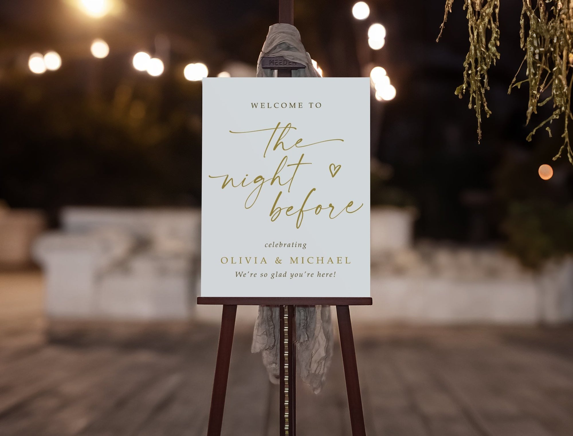 Rehearsal dinner welcome sign on an easel with decorative lights and plants in the background
