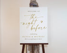White welcome sign with gold text saying "the night before" on an easel against a plain background