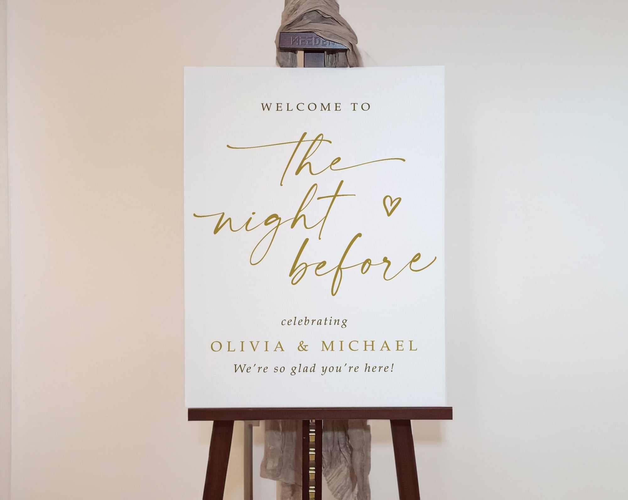 White welcome sign with gold text saying "the night before" on an easel against a plain background