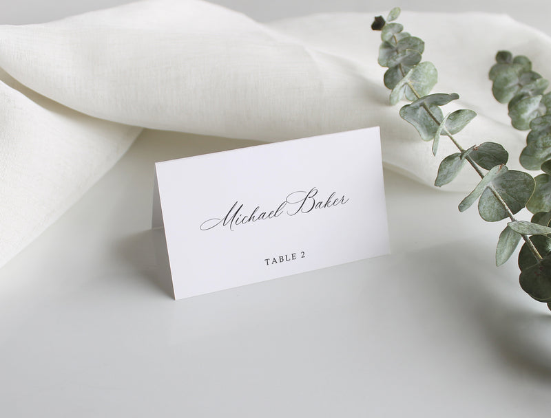 Classic wedding place card with guest name and table number, displayed with soft linens and eucalyptus accent.