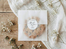 Baked goods in a clear packaging with a 'thank you' label on a wooden surface with flowers.