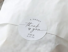 A round white paper wedding favor thank you sticker with elegant black script reading 'A SWEET thank you O & M 8.23.
