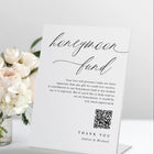 Standing “Honeymoon Fund” wedding sign with QR code in modern calligraphy, displayed on a reception table.