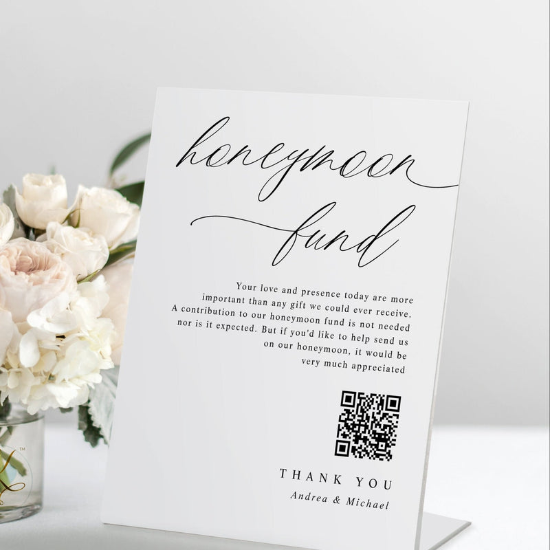 Standing “Honeymoon Fund” wedding sign with QR code in modern calligraphy, displayed on a reception table.