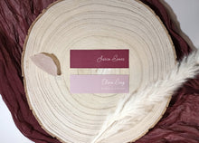 Two name cards on a wooden surface with feathers, placed on a maroon fabric background.