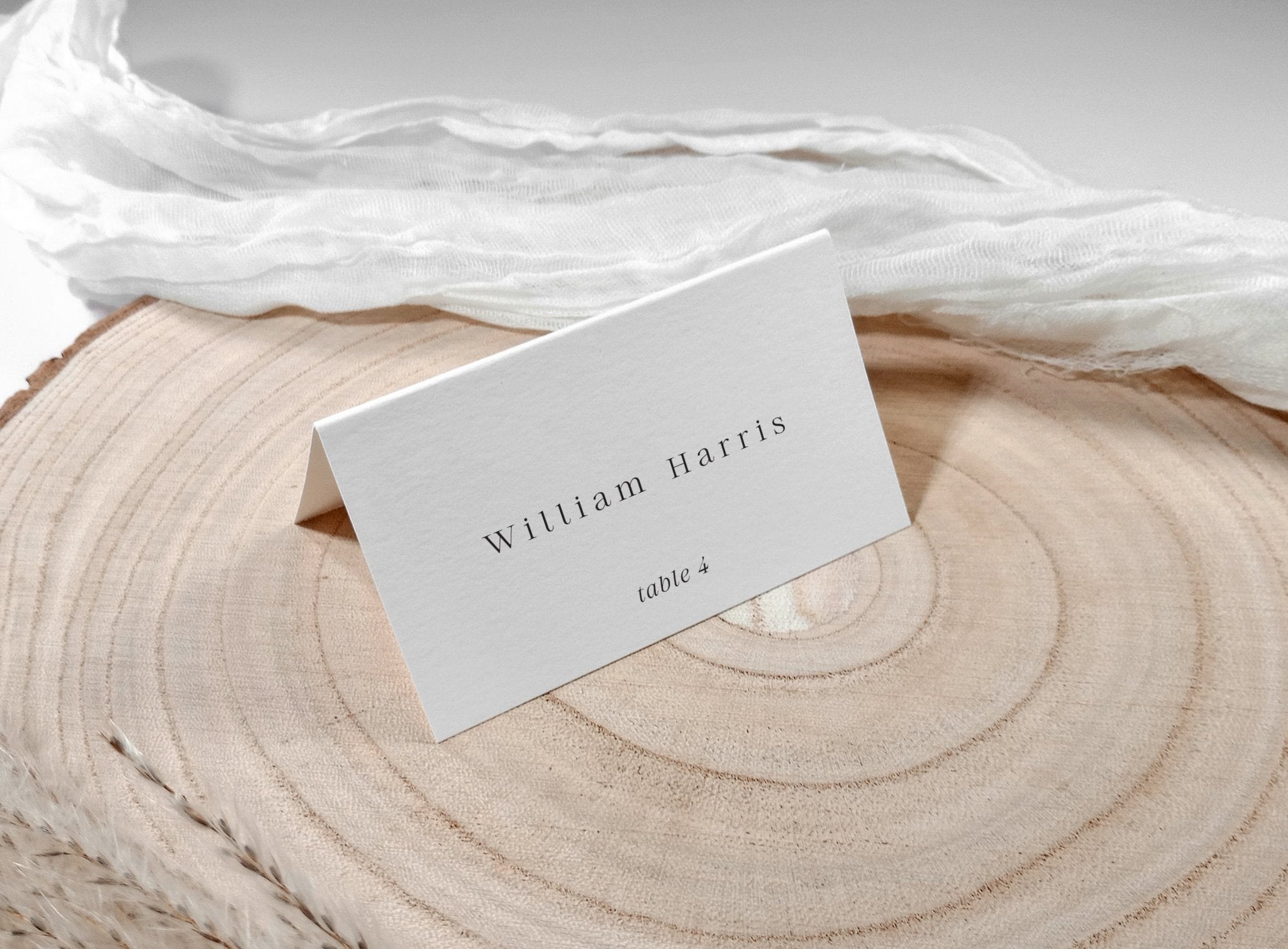 Minimalist name card with crisp black font, styled on white gauze and wood round for wedding place setting.