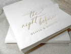 Personalized white cocktail napkin with gold foil names displayed on a linen tablecloth for a wedding rehearsal dinner.