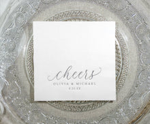 Personalized wedding napkin with “cheers” in silver foil on a clear glass plate