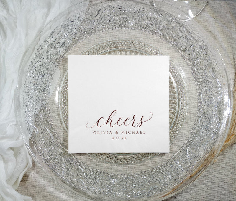 Close-up of swirly script “cheers” design in rose gold foil for a rehearsal dinner napkin
