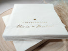 Close-up of “Cheers to Love” in gold foil on a modern white wedding cocktail napkin with playful script styling.