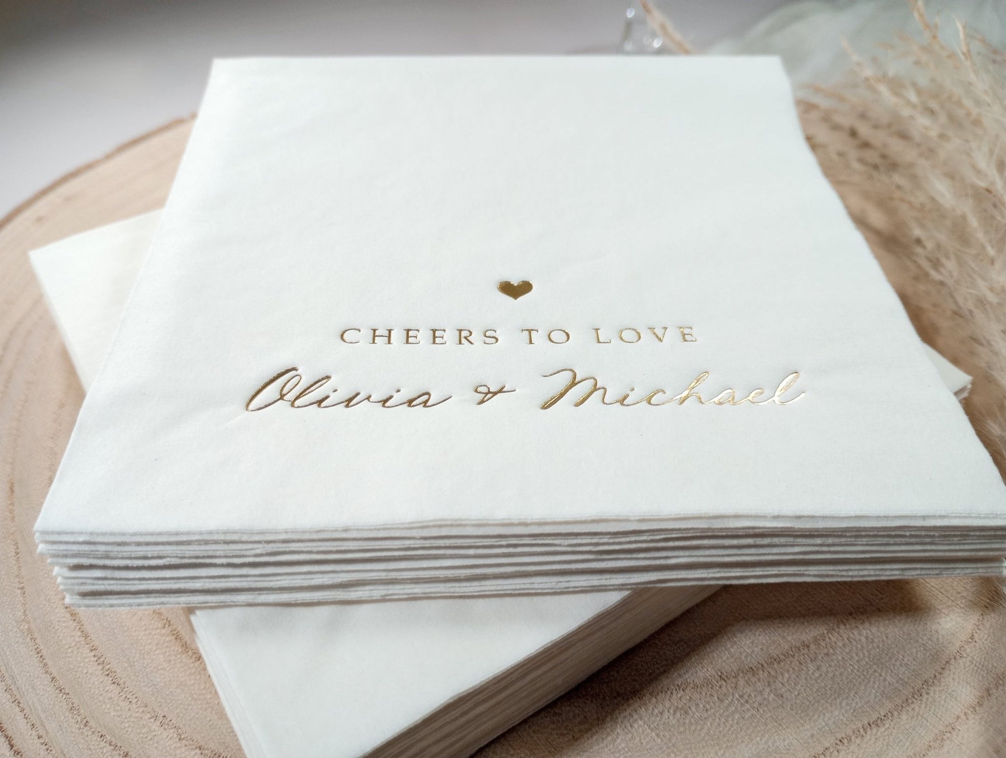 Close-up of “Cheers to Love” in gold foil on a modern white wedding cocktail napkin with playful script styling.