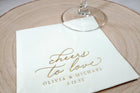 close up of gold foil personalized wedding napkins that say "cheers to love" in an elegant vintage script