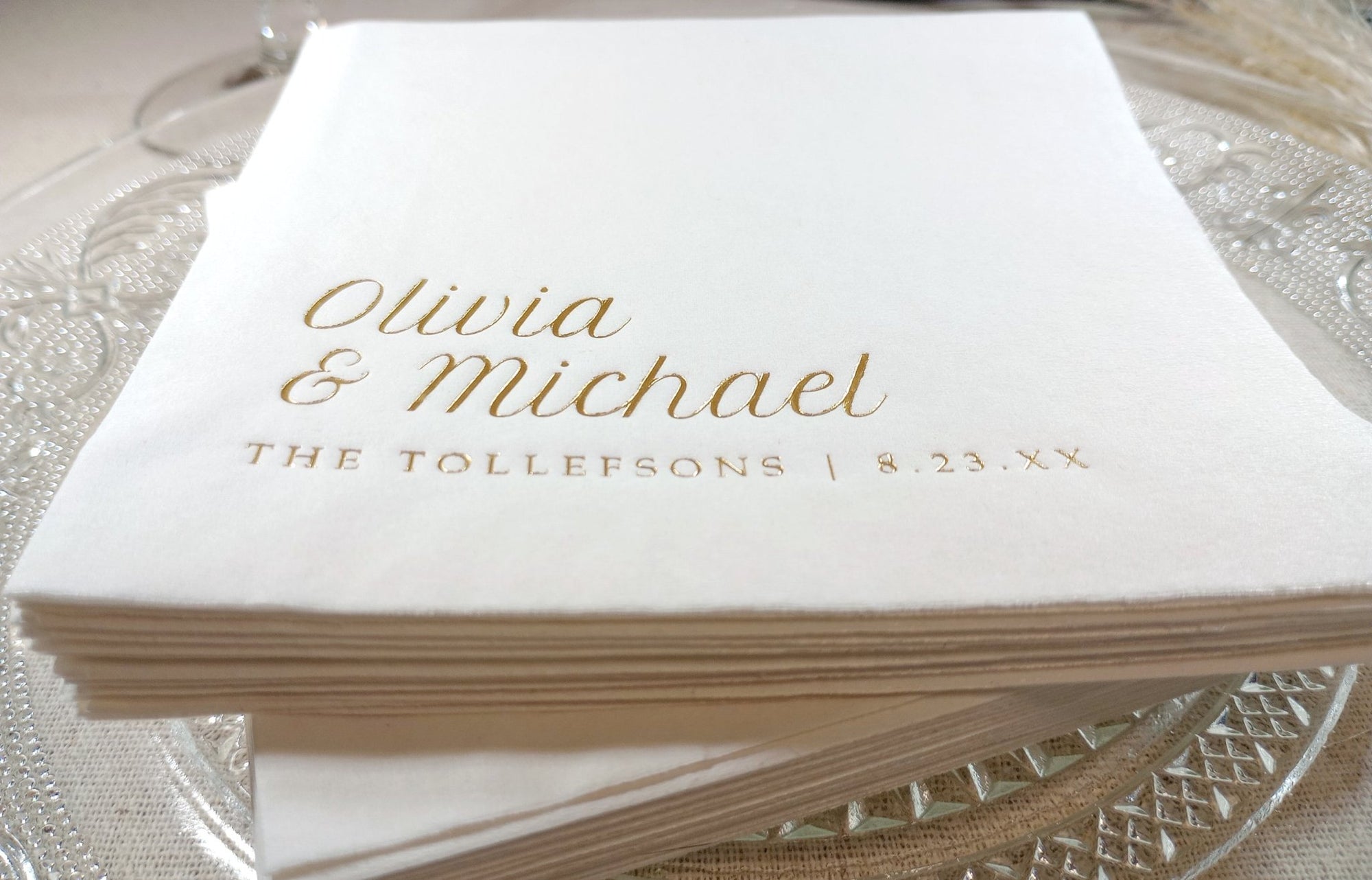 Stack of white napkins with gold text on a glass surface
