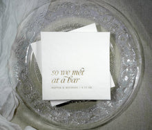 White wedding cocktail napkin with “So We Met at a Bar” in elegant gold foil and custom names below