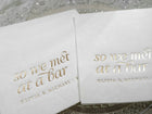 Close-up of gold foil stamped “So We Met at a Bar” napkins placed on a reception table setting