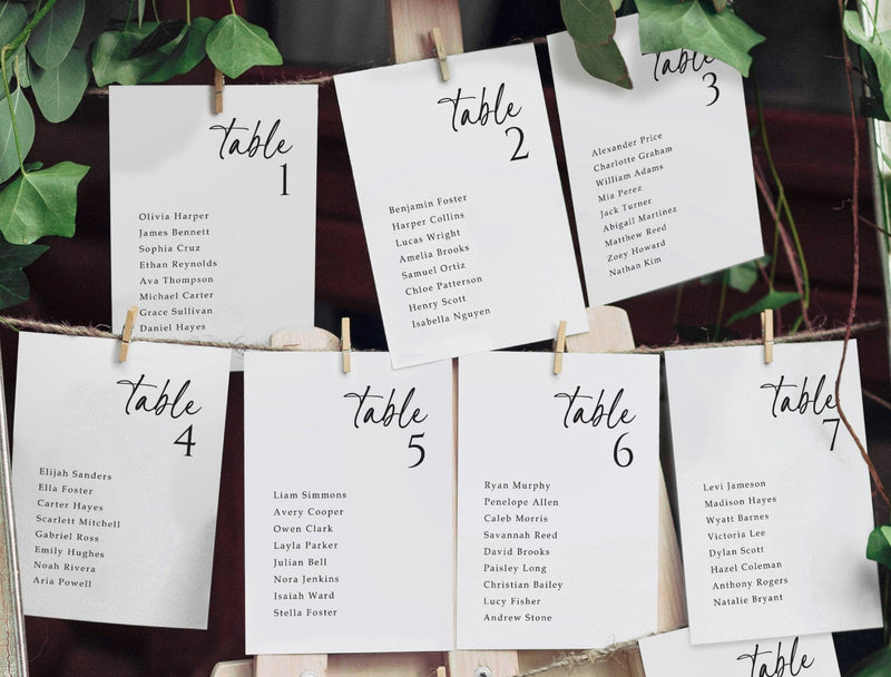 Seating arrangement cards for tables with names, pinned to a board with greenery.