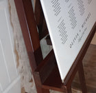 Wooden easel with a white board displaying text, a wedding seating chart, against a neutral background.