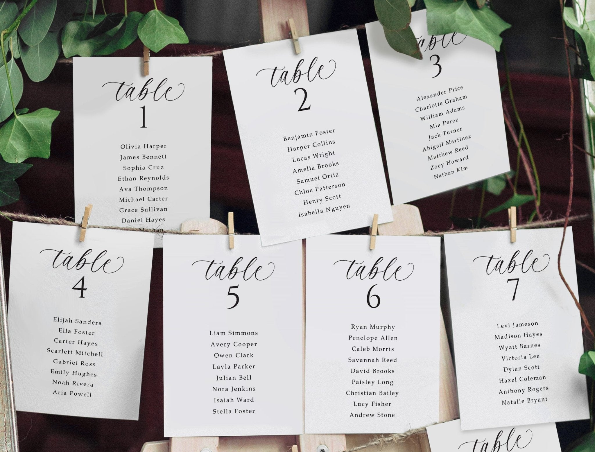 Seating arrangement cards for tables with names, pinned to a board with greenery.