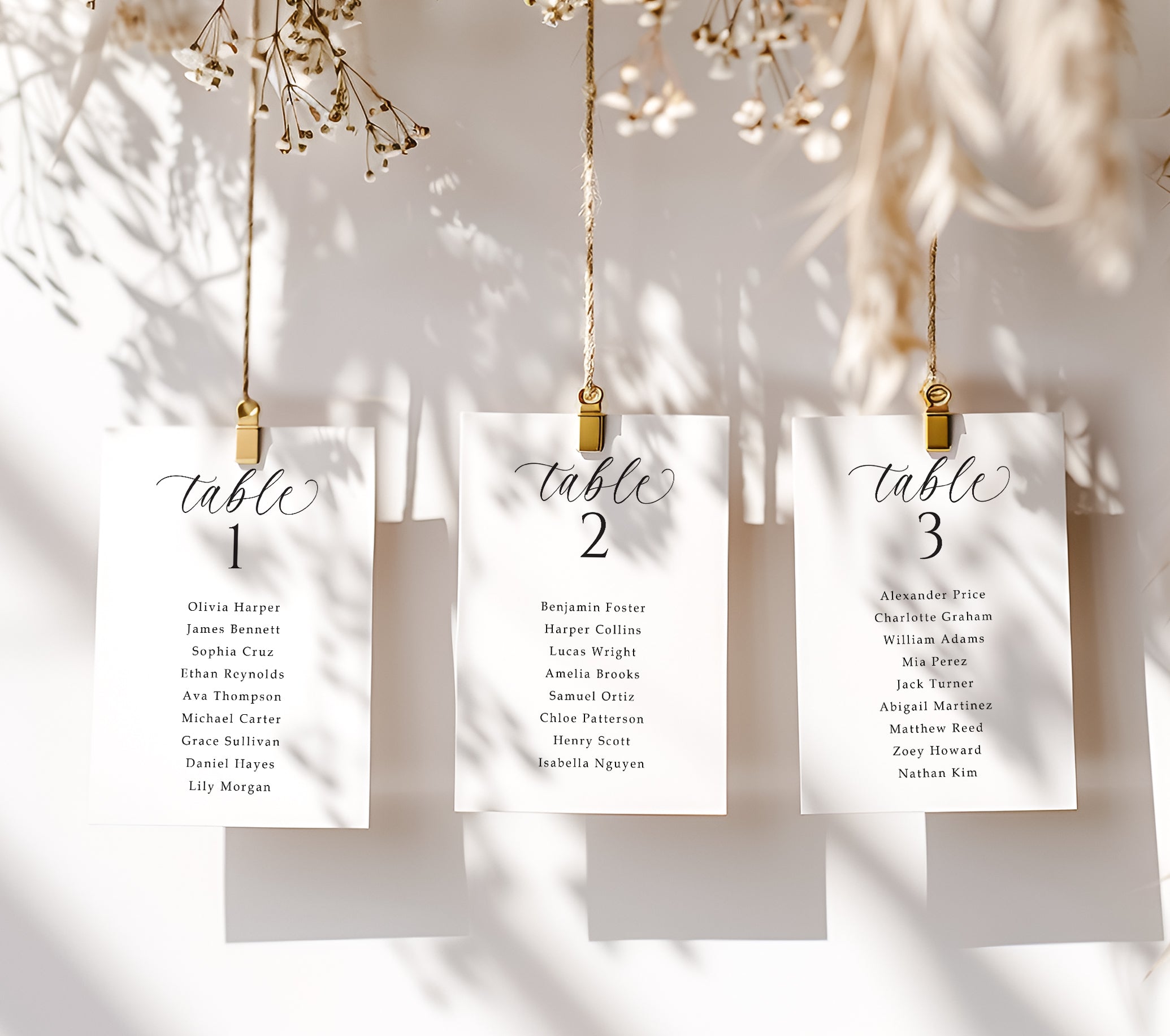 Three table assignment cards hanging on a string with gold clips against a neutral background.
