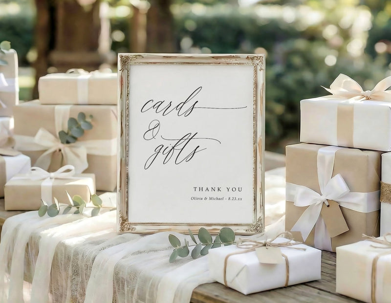 Custom printed wedding sign that says "cards & gifts" in an elegant calligraphy script and is personalized with the couple's names and wedding date. The sign is on a table surrounded by gifts in an outdoor setting.