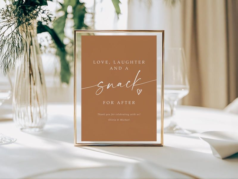 Framed wedding sign with 'Love, laughter and a snack for after' text on a table with decor.